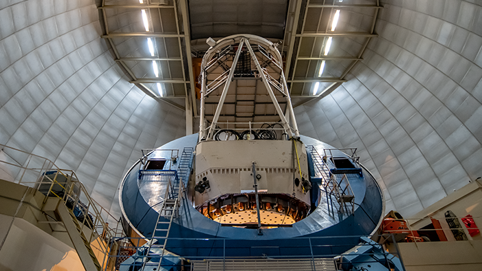 A blue telescope inside a dome. It consists of a square base on which sits a circular ring from which a thick cream coloured antennae protrudes.