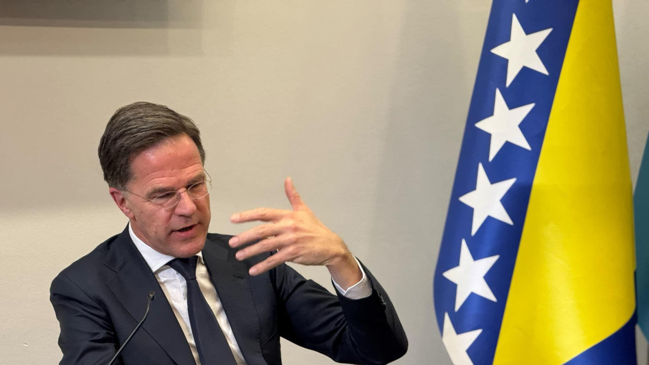 Mark Rute u poseti Sarajevu, sedi tokom konferencije, pored njega zastava BiH