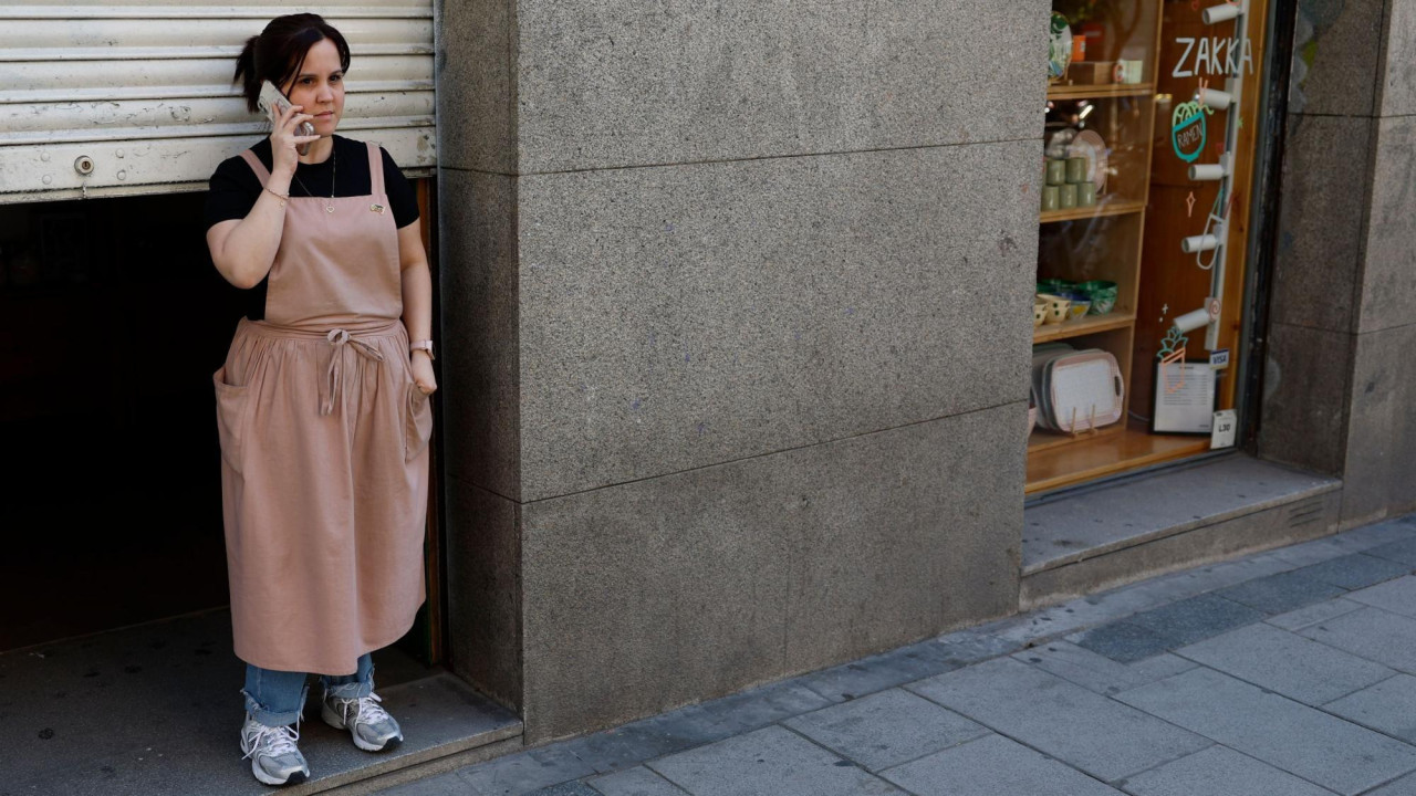 A woman stands beside a dark doorway of a closed shop in Spain